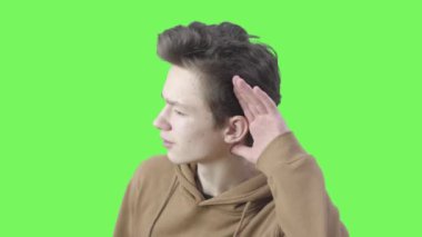 El ele tutuşup kameraya yaklaşan esmer çocuğun yan görüntüsü. Beyaz erkek gencin portresi yeşil ekran arka planında bir şey dinliyor. Chromakey, dikkat, işitme zorluğu.