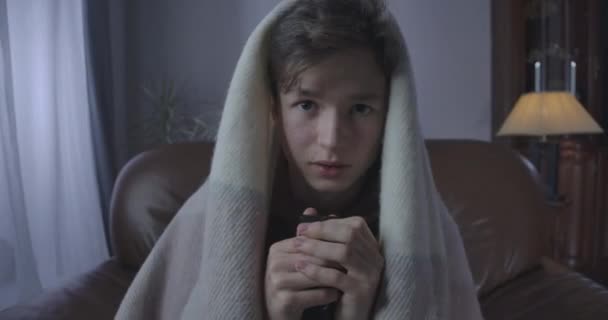 Portret van een bange tiener die 's avonds horrorfilms kijkt. Close-up van bange brunette Kaukasische jongen gewikkeld in een deken terug van TV. Angst, angst, levensstijl. Cinema 4k ProRes Hoofdkwartier. — Stockvideo