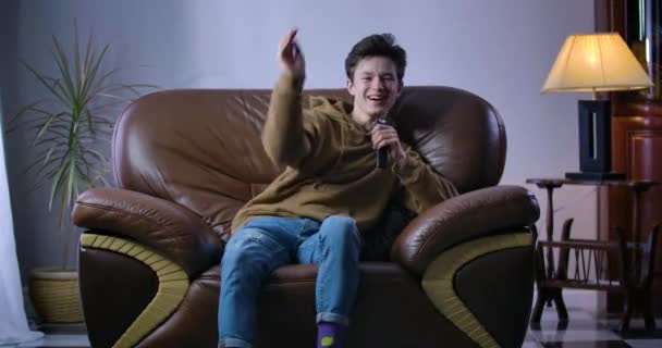 Joyeux garçon caucasien riant à haute voix comme assis sur un fauteuil avec télécommande. Joyeux adolescent regardant une émission de comédie ou un film à la télévision à la maison. Loisirs, détente, joie. Siège social Cinema 4k ProRes . — Video