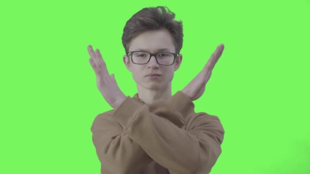 Poważny chłopak w okularach nie robi żadnego gestu na zielonym tle. Portret pewnego siebie białego nastolatka nie zgadza się z czymś. Sprzeciw, protest, dezaprobata. Chromakey. — Wideo stockowe