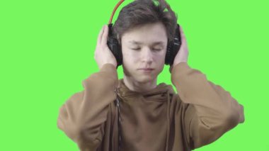 Kafkasyalı üzgün çocuğun portresi kulaklıkla sakin klasik müzik dinliyor. Kahverengi gözlü esmer ergenin yakın çekimi kulaklıkla melodinin tadını çıkarıyor. Hobi, yaşam tarzı. Kromakey arkaplanı.