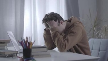 Kafası el ele tutuşan stresli beyaz çocuk dizüstü bilgisayarın önünde oturuyor. Depresyondaki üniversite öğrencilerinin kişisel sorunları ya da çalışma güçlüklerinin yan görüntüsü. Yaşam tarzı, stres.