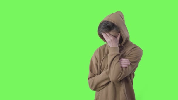 Zoufalý kavkazský teenager si třel spánky a vzdychal. Střední záběr smutného chlapce v kapuci pózujícího na zeleném pozadí. Stres, dospívání, problém, životní styl. Chromakey. — Stock video