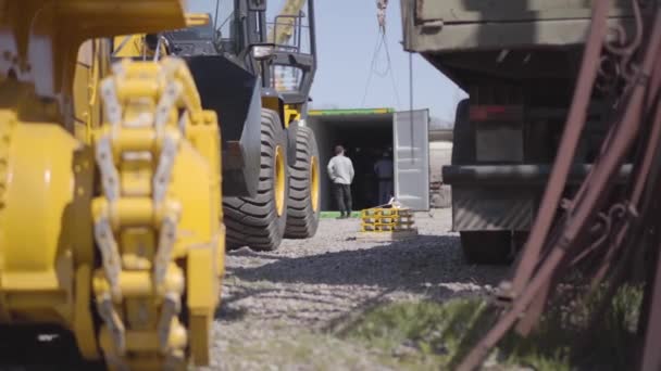 Trabajadores de la construcción caucásicos revisando el equipo en el contenedor de envío en el fondo como maquinaria industrial pesada de pie al aire libre en la parte delantera. Fabricación, negocio, industria . — Vídeo de stock