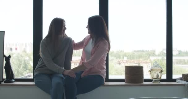 Retrato de vista lateral de lésbicas caucasianas sentadas no parapeito da janela e conversando. Feliz casal caucasiano do mesmo sexo desfrutando de tempo juntos em casa. Amor, estilo de vida, família LGBT. Cinema 4k ProRes HQ . — Vídeo de Stock