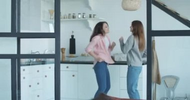Lezbiyen çiftin mutfakta eğlenceli enerjik dansı. Evde dans eden iki güzel beyaz kadının portresi. LGBT ailesi, aynı cinsiyet ilişkisi, mutlu homoseksüel çift. Sinema 4k ProRes Merkezi