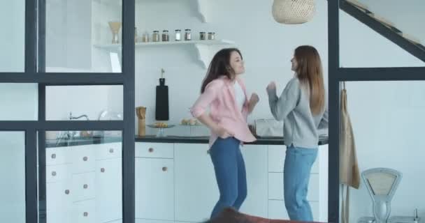 Divertente danza energetica di coppia lesbica in cucina. Ritratto di due belle donne caucasiche allegre che ballano a casa. Famiglia LGBT, stesso rapporto sessuale, coppia omosessuale felice. Cinema 4k ProRes HQ — Video Stock