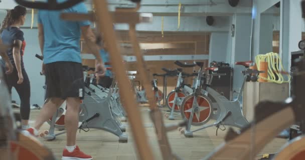 Sportovní běloši muži a ženy vstupují do tělocvičny a začínají jezdit na kole. Sportovní cvičení skupiny mladých lidí na cvičných kolech. Sport, zdravý životní styl, svalnatá stavba. Cinema 4k ProRes HQ. — Stock video