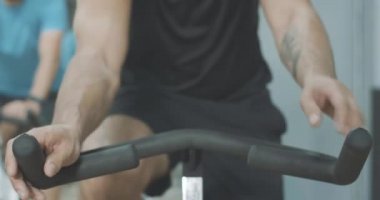 Elinde dövmesi olan, avuç içlerini gidona koyan tanınmamış beyaz bir sporcu. Spor salonunda bisiklete binen güçlü genç adam. Sağlıklı yaşam tarzı, bisiklet, eğitim kavramı. Sinema 4k ProRes Merkezi.