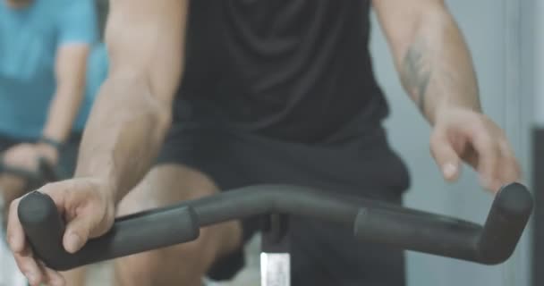 Sportivo caucasico irriconoscibile con tatuaggio a mano che mette le palme sul manubrio. Forte giovane in sella cyclette in palestra. Concetto di stile di vita sano, ciclismo, allenamento. Cinema 4k ProRes HQ . — Video Stock