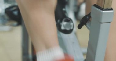 Spor kulübünde pedal çeviren beyaz erkek bacaklarının yakın çekimi. Spor aletleriyle spor salonunda bisiklete binen tanınmamış bir sporcu. Antrenman, egzersiz, spor. Sinema 4k ProRes Merkezi.