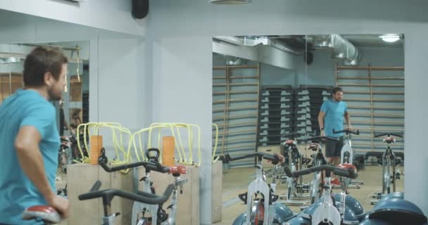 Веселий кавказький тренер вітає чоловіків і жінок у спортзалі. Групи здорових струнких людей починають тренуватися на велосипедах у спортивному клубі. Особиста підготовка, спосіб життя, спорт. Фільм 4k ProRes HQ. — стокове відео