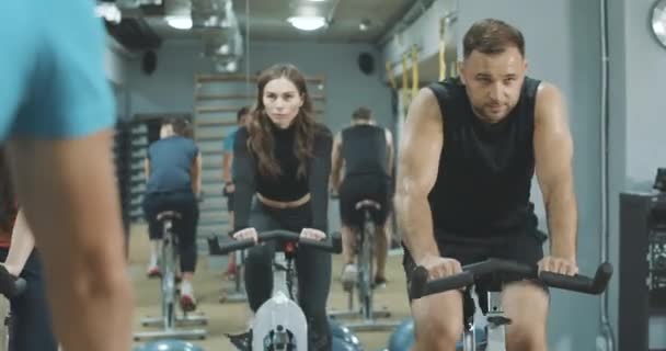 描述筋疲力尽的男人和女人在健身房骑自行车的样子。与教练一起在跑车上训练汗流浃背的运动员的前景色.生活方式，运动。Cinema 4k ProRes HQ. — 图库视频影像
