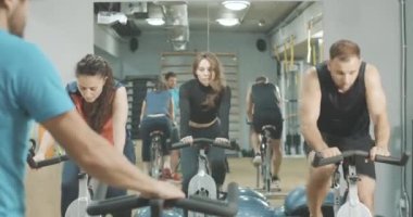 Antrenörün spor kulübündeki insanlara bisiklet ekipmanları hakkında bilgi verdiği arka plan. Spor salonunda spor yapan genç erkek ve kadınlar, koçun desteğiyle bisiklet sürüyorlar. Spor konsepti. Sinema 4k ProRes Merkezi.