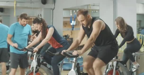 Professional trainer correcting training of people in gym. Exhausted man and slim women riding exercise bikes. Sportive people exercising indoors. Sportive lifestyle. Cinema 4k ProRes HQ. — Stock Video