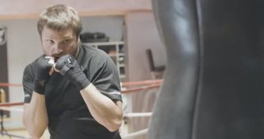 Spor salonunda profesyonel boks boks torbası portresi. Genç, sakallı, beyaz adam teçhizatlı eğitim görüyor. Spor, kickboks, dövüş sanatları, sağlıklı yaşam tarzı. Sinema 4k ProRes Merkezi.