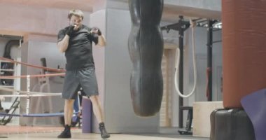 Spor salonunda boksörlerin kum torbasıyla dövüştüğü geniş açı. Kafkas esmer adamın spor kulübündeki eğitiminin portresi. Sağlıklı yaşam tarzı, spor, güç, dövüş sanatları. Sinema 4k ProRes Merkezi.