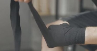 Boks bandajı süren beyaz erkek ellerinin yakın çekimi. Spor salonunda siyah bantla bileğini saran tanınmamış yetişkin bir sporcu. Spor, dövüş sanatları, yaşam tarzı. Sinema 4k ProRes Merkezi.