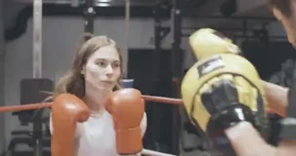 Live-Kamera, selbstbewusste junge Boxerin beim Training mit Trainer im Fitnessstudio. Porträt einer schönen kaukasischen Frau, die Trainingshandschuhe schlägt. Sparring aus Trainer und Student. Cinema 4k ProRes Hauptquartier. — Stockvideo