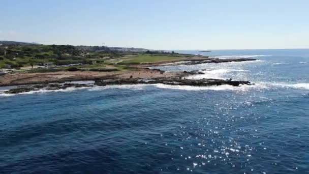 Drohne bewegt sich entlang der sonnigen Küste, Blick vom Meer aus. Luftaufnahme der zyprischen Mittelmeerküste. Dunkelblaue Wellen wälzen sich am Strand und krachen mit Schaum. Natur, Meer, Schönheit. — Stockvideo