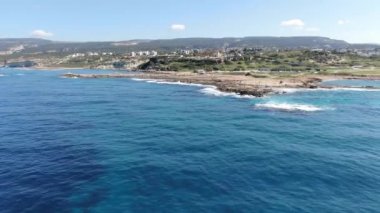 Kıbrıs Rum Kesimi 'nin Akdeniz kıyısındaki turizm beldesinin geniş bir görüntüsü. Kumlu ve kayalık kıyı şeridi olan yeşil tepelere dağılmış küçük binaların hava manzarası. Yaz güneşinin altında mavi deniz suları.