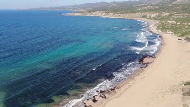 Uitzicht vanuit de lucht op de blauwe lagune met rondom groene zandheuvels. Koude golven rollen op het strand en crashen met schuim. Brede opname van Cyprus resort aan de Middellandse Zee. Paradijs, zeegezicht, natuur. — Stockvideo