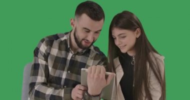Neşeli beyaz adam ve kız tablet kullanıyor, konuşuyor ve gülüyorlar. Olumlu genç adam ve genç kız internette sörf yaparken eğleniyorlar. Boş zaman, aile, yaşam tarzı. Yeşil ekran. Sinema 4k ProRes Merkezi.
