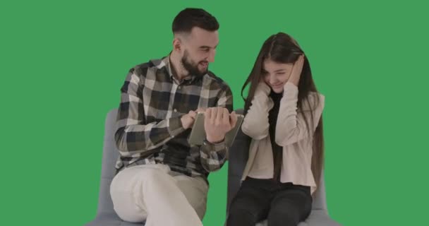 Portret van vrolijke vader en tienerdochter met behulp van tablet op groene achtergrond. Grappig brunette Kaukasisch meisje zit met oren gesloten met handen terwijl de man praat. Cinema 4k ProRes Hoofdkwartier. — Stockvideo