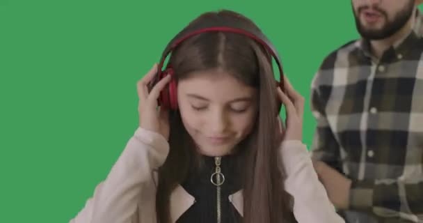 Close-up dari remaja riang di headphone dengan pria berjanggut kabur berbicara di latar belakang. Tersenyum gadis Kaukasia mengabaikan ayah mendidiknya. Chromakey, masa remaja. Sinema 4k ProRes HQ. — Stok Video