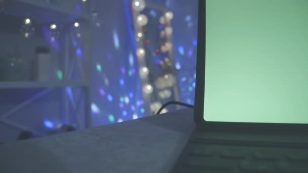 Laptop mit grünem Bildschirm auf der rechten Seite, im Hintergrund funkeln bunte Lichter. Feiern, Feiern, Spaß, Freizeit. — Stockvideo