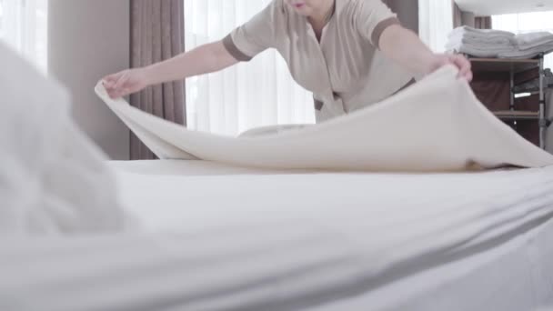 Vážná kavkazská dospělá žena v uniformě narovnávající pokrývku na velké posteli. Portrét sebevědomé profesionální služebné, jak stele postel v hotelovém pokoji. Profesionalita, životní styl, služby, cestovní ruch. — Stock video