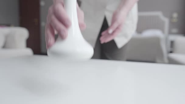 Main féminine mettant vase et tasse à café à la table blanche. Femme caucasienne méconnaissable en uniforme de femme de ménage nettoyage chambre d'hôtel. Service, mode de vie, tourisme, profession, emploi . — Video