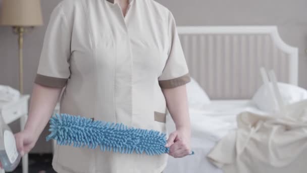 Onherkenbaar dienstmeisje in uniform met stofborstel en vloeibare reiniger. Chubby blanke vrouw staat in de hotelkamer met schoonmaak apparatuur. Service, netheid, netheid, toerisme. — Stockvideo