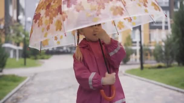 Joyeux petite fille caucasienne qui tourne parapluie à l'extérieur. Portrait d'un enfant mignon souriant profitant du printemps ou de l'automne après la pluie. Joie, enfance, bonheur, mode de vie . — Video