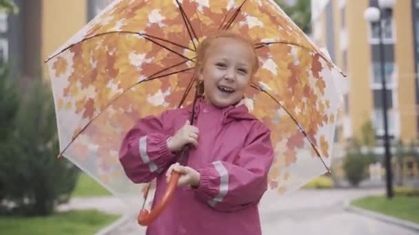 Śmiejąca się biała dziewczynka stojąca na zewnątrz i trzymająca parasol. Portret blond szczęśliwego dziecka cieszącego się deszczowym dniem. Wypoczynek, dzieciństwo, styl życia, radość. — Wideo stockowe