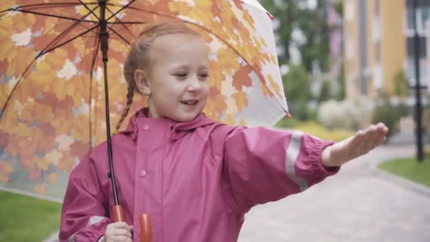 Bonita niña rubia con paraguas chequeando lluvia con palma. Retrato de niño caucásico lindo de pie al aire libre con la mano estirada y sonriente. Temporada de lluvias, estilo de vida, infancia, ocio . — Vídeos de Stock