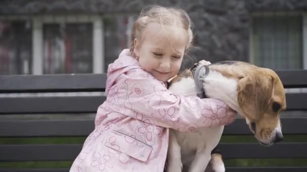 Feliz chica linda abrazando perro adorable. Retrato de niño caucásico alegre abrazando encantadora mascota al aire libre y sonriendo. Alegría, ocio, infancia, estilo de vida, cuidado, felicidad . — Vídeo de stock