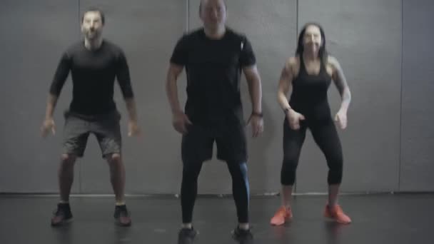 Trois caucasiens sportifs souriants sautant de haut en bas dans la salle de gym. Portrait de jeunes hommes et femmes joyeux faisant de l'exercice à l'intérieur. Fitness, sport, endurance, mode de vie sain . — Video