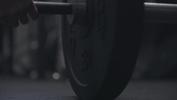 Close-up van een lange halter die op de grond valt in een donkere sportschool. Onbekende sportman die gewichten gooit. Lichaamsbouw, uithoudingsvermogen, training, oefening, levensstijl. — Stockvideo