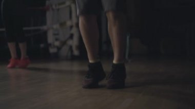 Koyu renk spor salonunda ip atlayan beyaz erkek ayaklarına yakın çekim. Arka planda egzersiz yapan tanınmamış genç bir kadın. Fitness, spor, yaşam tarzı, egzersiz.
