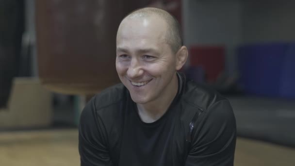 Närbild porträtt av glada vuxna kaukasiska idrottsman talar med någon i gymmet. Glad man med bruna ögon vilar i sportklubben och ler. Glädje, paus, sport, livsstil. — Stockvideo