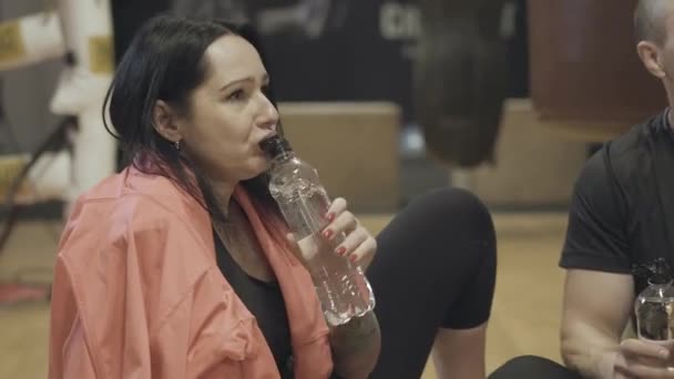 Радісна кавказька жінка п "є воду і розмовляє з друзями в спортзалі. Порушення атлетичних молодих людей у фітнес-клубі. Спосіб життя, спорт, відпочинок, тренування. — стокове відео