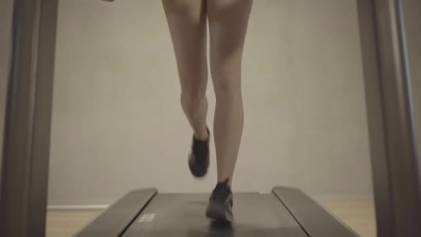 Κάμερα κινείται προς τα πάνω από τα θηλυκά λεπτά πόδια τζόκινγκ στο διάδρομο στο πρόσωπο της αυτοπεποίθηση ξανθιά καυκάσια γυναίκα κατάρτισης στο γυμναστήριο. Πορτρέτο της λεπτής ελκυστική νεαρή αθλήτρια άσκηση στο γυμναστήριο. — Αρχείο Βίντεο