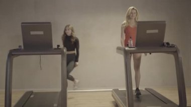 Kendine güvenen iki zayıf kadın spor salonunda antrenman yapmaya başlıyor. Çekici sarışın ve esmer beyaz kızın portresi. Ekipmanları açıyor ve koşuyor. Güzellik, sağlık, spor, yaşam tarzı.