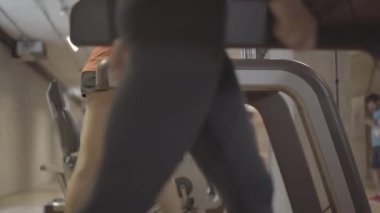 Spor salonunda koşu bandında yürüyen beyaz kadın bacakları. Beden eğitimi kulübünde ekipman üzerinde dolaşan tanınmayan iki genç kadının yan görüntüsü. Spor, egzersiz, eğitim, yaşam tarzı.