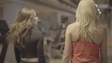 Kamera spor salonunda yürüyen ve sohbet eden genç kadınları çekiyor. fitness kulübünde konuşan sarışın ve esmer beyaz kadın sporcuları görüyorum. Sağlık, güzellik, yaşam tarzı, spor.