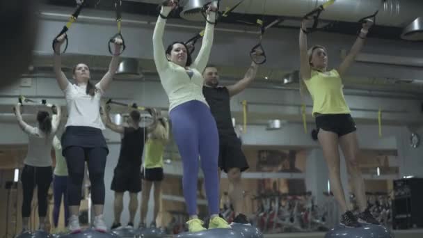 Treino TRX de jovens atletas caucasianos no ginásio. Tiro largo de quatro mulheres e homens treinando em clube de fitness. Esporte, estilo de vida saudável, resistência, exercício . — Vídeo de Stock