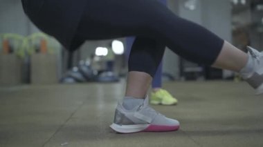 Tanımlanamayan bir kadının spor salonunda TRX tek bacağı üzerinde oturuşunun yan görüntüsü. Spor salonunda kişisel antrenörle antrenman yapan beyaz bir kadın. Güç, atletizm, spor, yaşam tarzı.