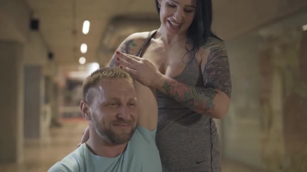 Mujer positiva ayudando a hombre sonriente en estiramiento. Entrenamiento entrenador personal deportista caucásico en el gimnasio. Deporte, bienestar, estilo de vida saludable, disfrute . — Vídeos de Stock