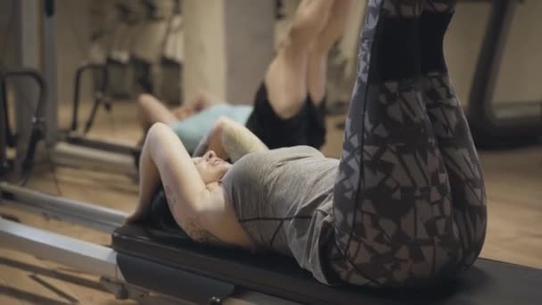 Kaukasisk kvinna som höjer benen i gymmet och pratar som en suddig man som repeterar träning. Vuxen kvinnlig tränare tränar med manlig idrottsman i gym. Livsstil, hälsa, sport, fitness. — Stockvideo